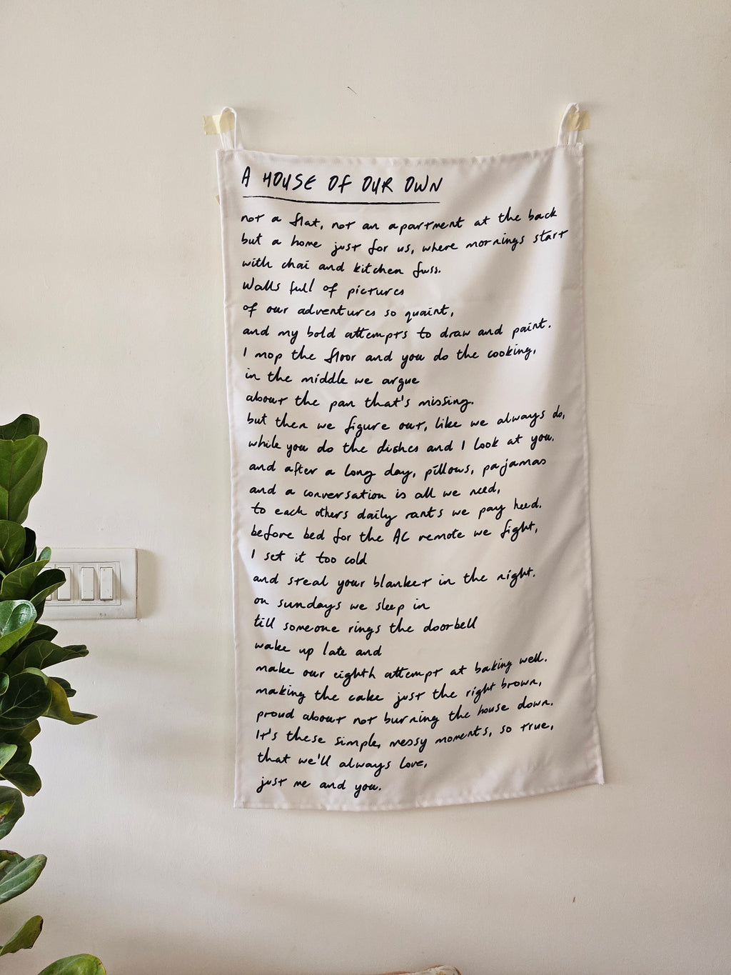 Minimalist beige cotton wall hanging with embroidered house illustration and quote, displayed on a clean white background.