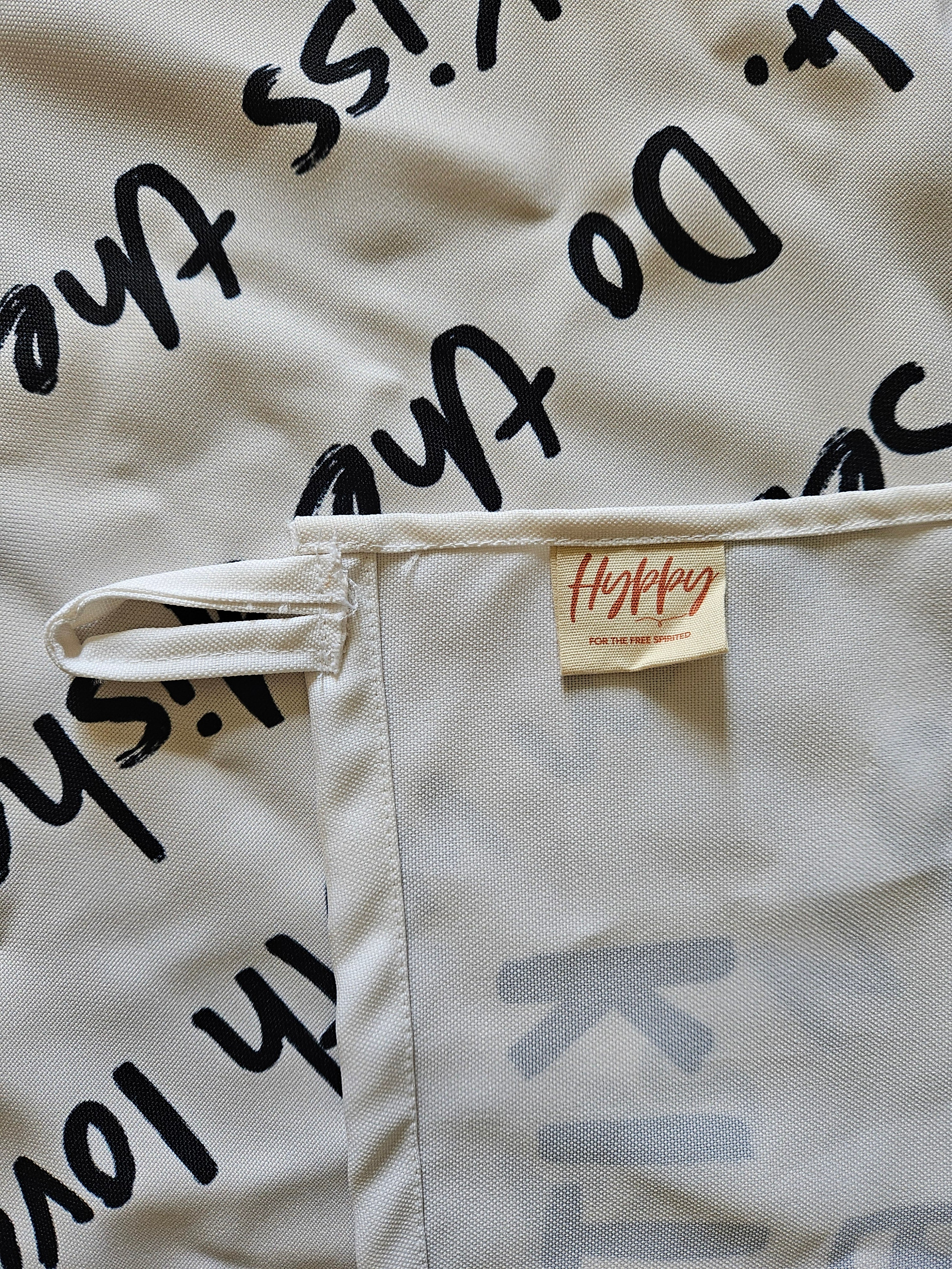 Detailed close-up of black embroidered quote and hand-drawn house on beige cotton fabric with neat stitching.

