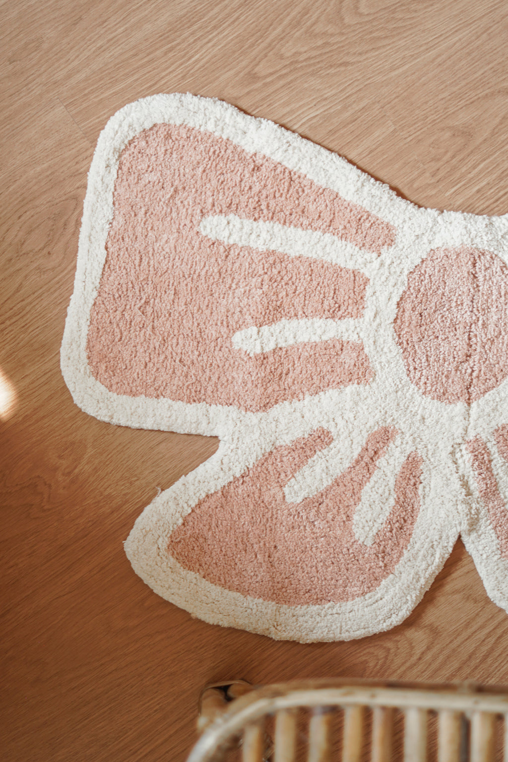 Close-up of blush pink embroidery and soft fabric texture on the bow-shaped rug.

