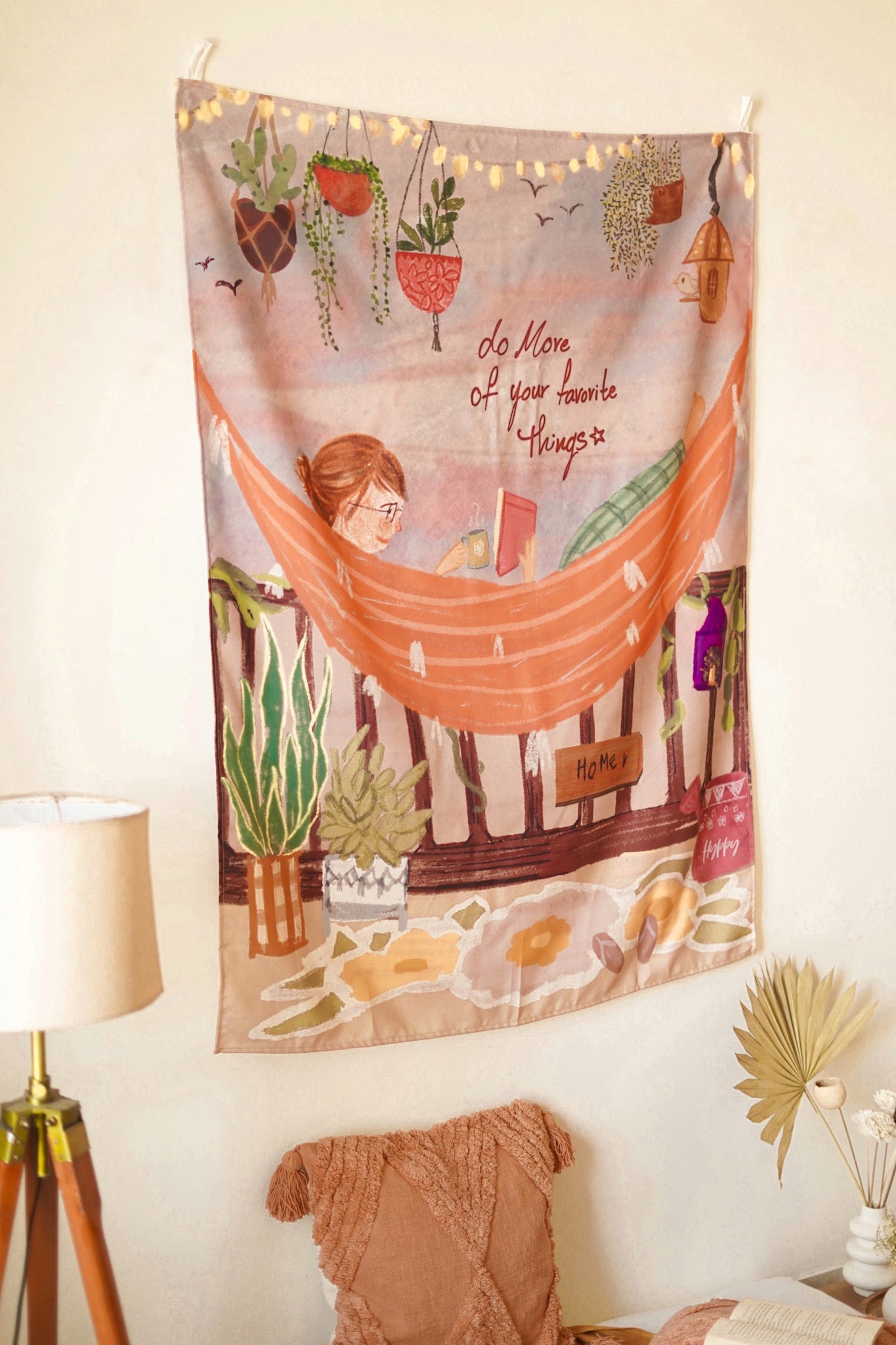 Boho-style illustrated wall hanging styled above a wooden desk with books and a lamp for cozy room decor.

