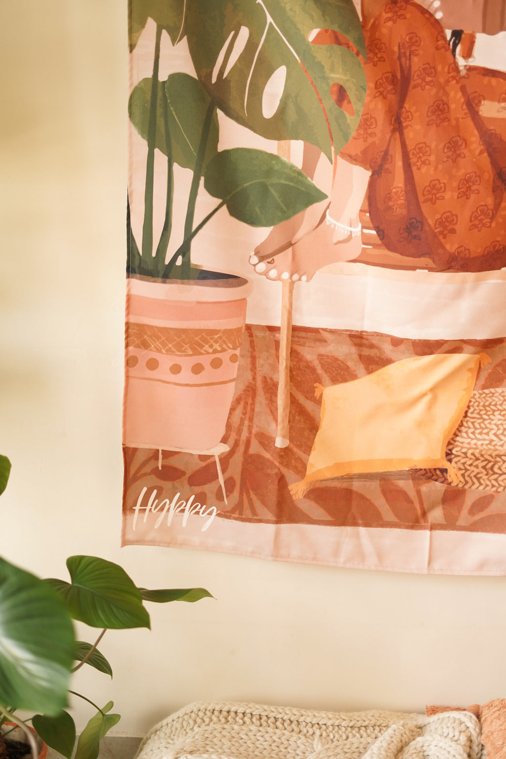 Close-up of the Boho Tapestry's design, highlighting the warm color palette and bohemian elements like indoor plants and stacked books.

