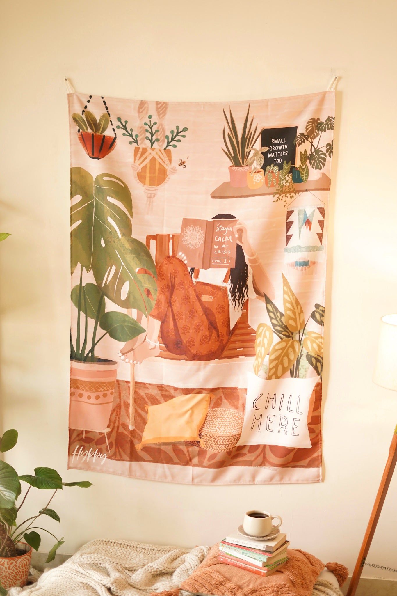 Full view of the Boho Tapestry hanging on a neutral-toned wall, featuring a cozy reading nook with plants, books, and a "Chill Here" cushion image.

